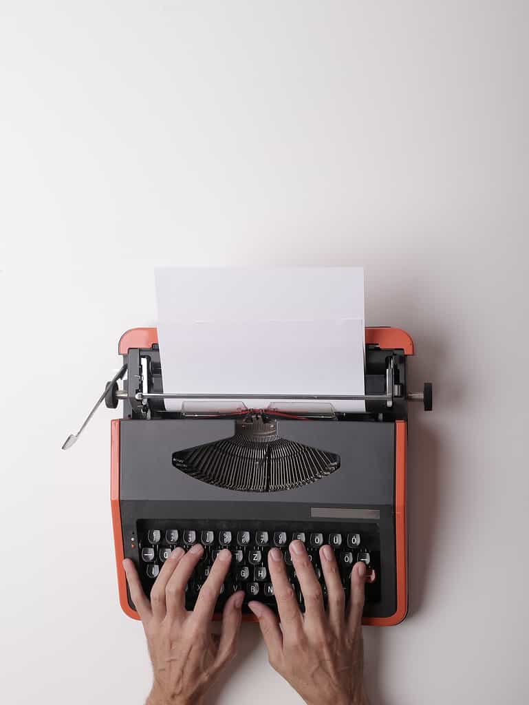From above crop person using vintage black and red typewriter with white blank sheet of paper against white background